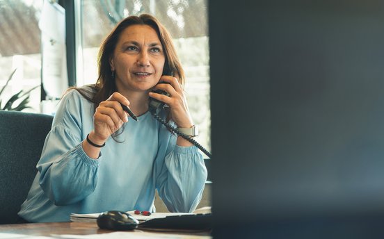 Frau mittleren Alters sitzt am Schreibtisch und telefoniert